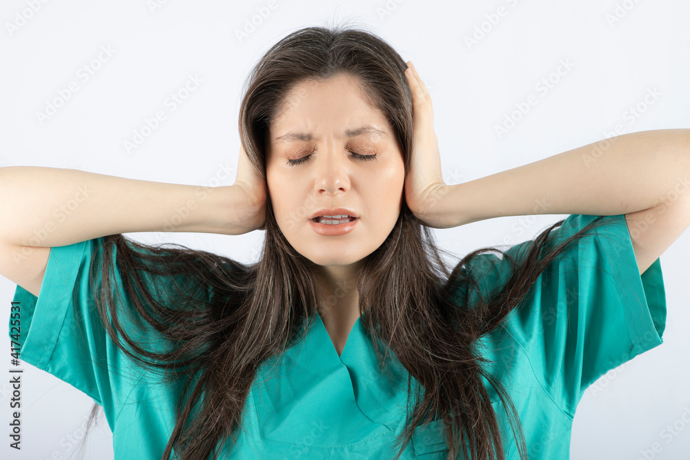 Tired female nurse covering her ears on white background