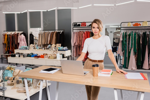 Seller standing near laptop, notebook and accessories in showroom