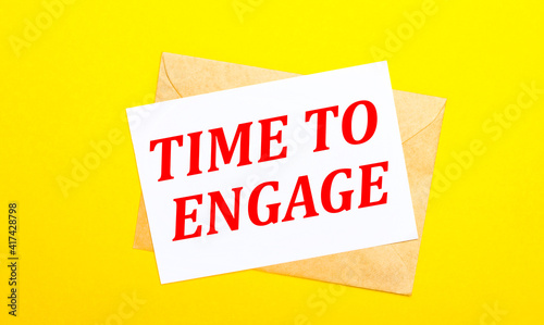 On a yellow background, an envelope and a card with the text TIME TO ENGAGE. View from above