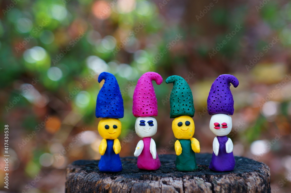 Figures of four fairy-tale dwarfs made of plasticine in the forest on a colored background.