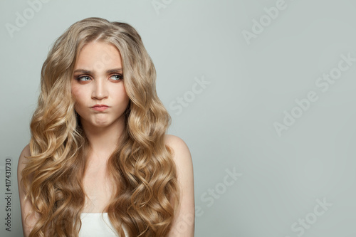 Funny blonde woman with long curly hair grimacing on white background