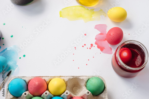 DIY egg dying set, tray of colored easter eggs on white background with paint splashes. Flat lay.