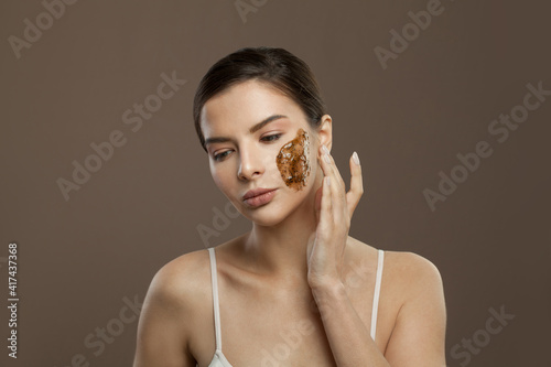 Beautiful woman applying scrub to the skin on brown background, skin and body care concept