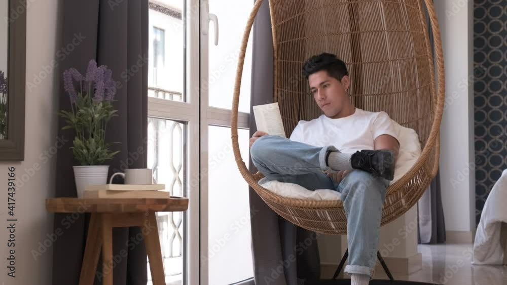 Portrait of young man reading a book while sitting in a comfortable chair at home.
