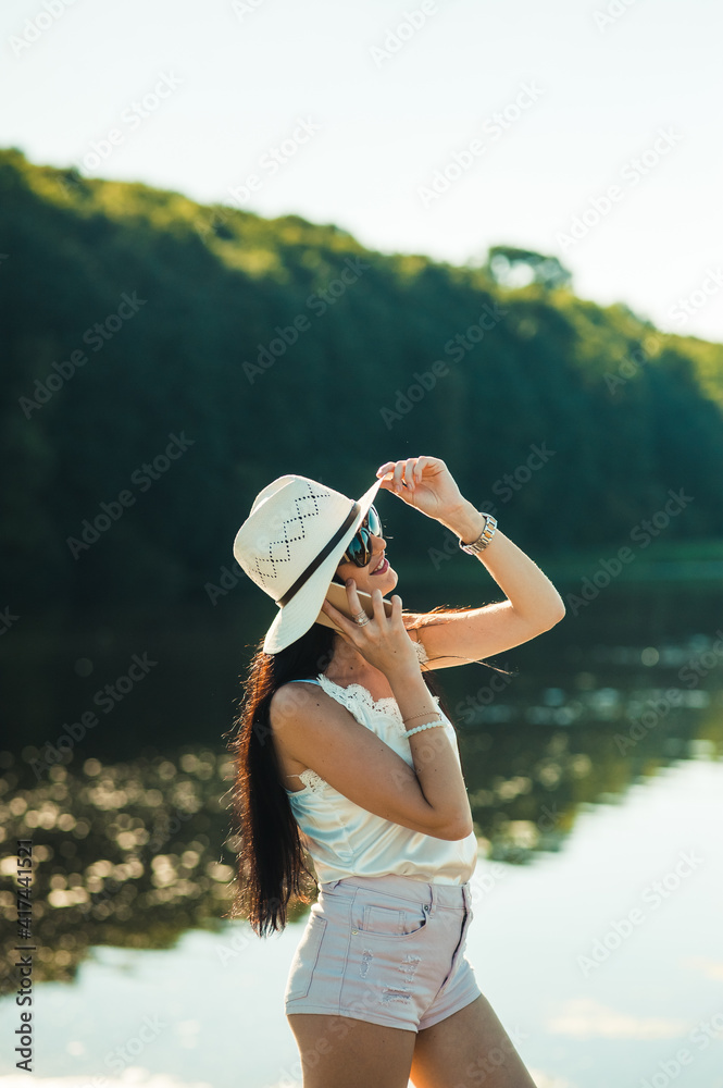 Fototapeta premium Sexy girl talking on the phone in the park.Gorgeous slender brunette talking on the phone by the lake.Smiling woman talking outdoors.