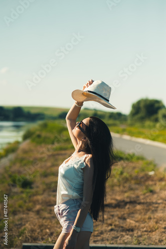 Sexy girl holding a hat in her hands in the park.Portrait of the beautiful girl, smiling for the photo. She is wearing sunglasses and holding her hat in her hands.