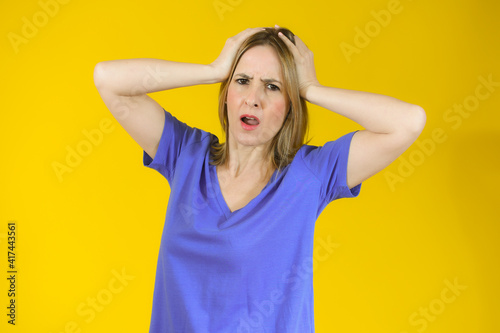 Shocked amazed young woman with hands on head standing over yellow background