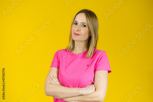 Portrait of a smiling young woman standing with arms folded isolated over yellow background
