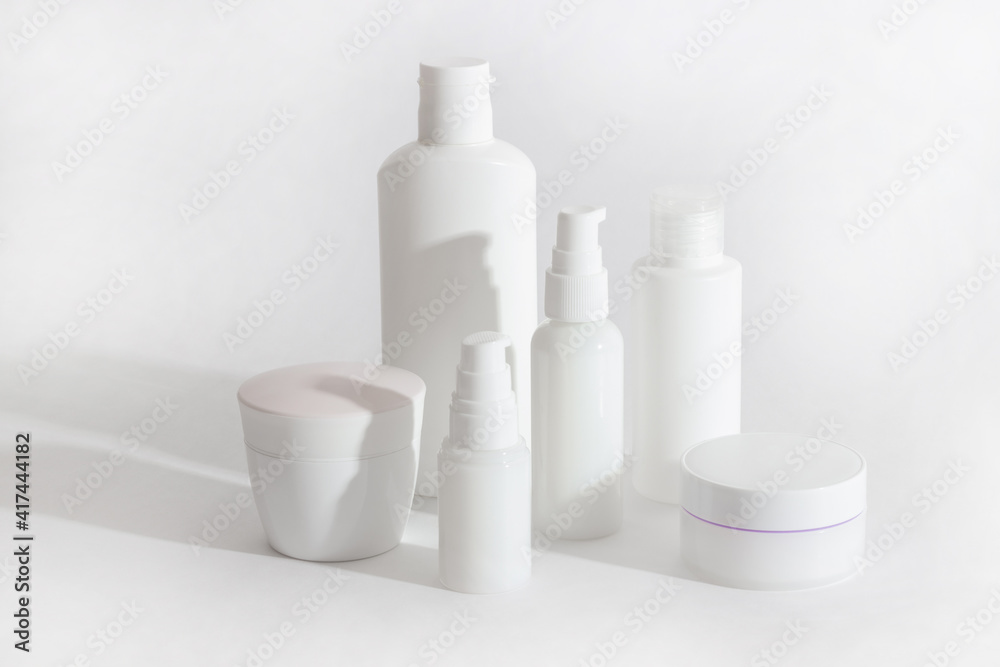 Set of white cosmetic bottles and jars with hard shadows. Home and beauty salon care concept Set of white cosmetic bottles and jars with hard shadows. Home and beauty salon care concept