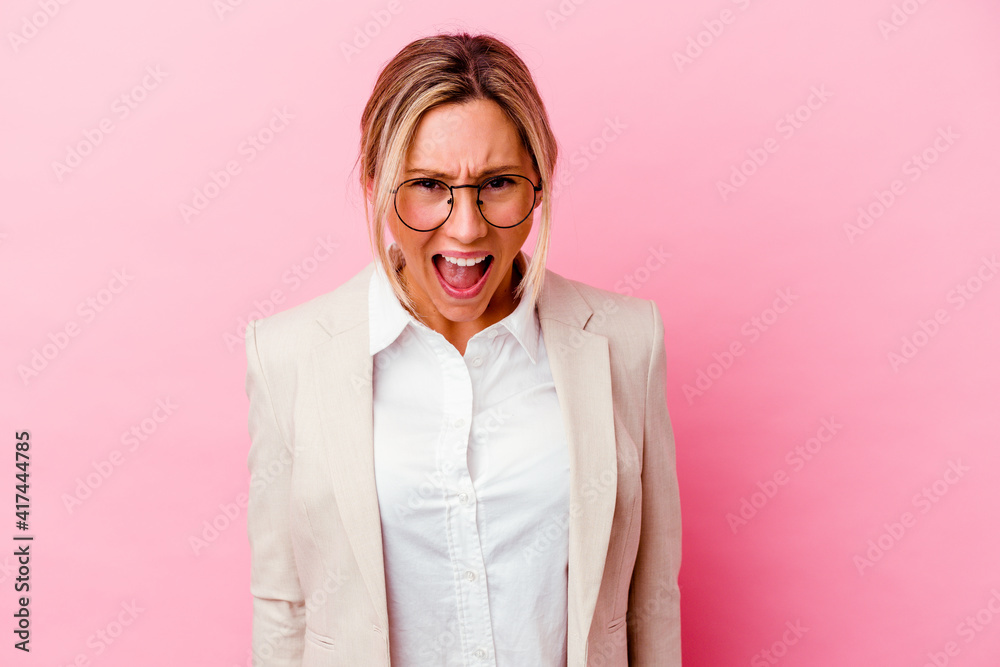 Young caucasian mixed race business woman isolated on pink background screaming very angry and aggressive.