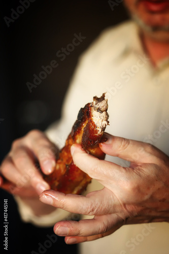 The man is eating fried pork ribs. Man bites meat. Unhealthy food.