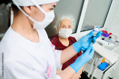 a nurse wearing a mask and rubber gloves is preparing to vaccinate an elderly woman against viral diseases. Prevention of coronavirus infection