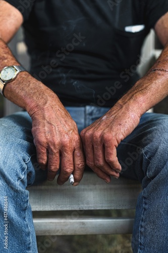 Stop smoking cigarettes concept. Portrait of rugged older man holding a cigarette in rough wrinkled hands. Bad habits of smoking.