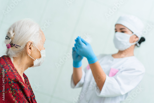 A doctor wearing rubber gloves prepares to inject an elderly woman in the hospital. A nurse holds a syringe before making a vaccine against Covid-19 or coronavirus.