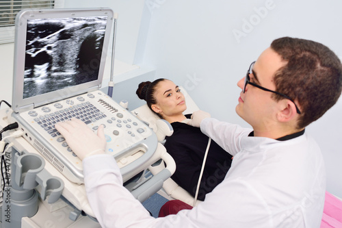 the doctor performs an ultrasound examination of the thyroid gland of a young, pretty woman in a modern clinic. Prevention of thyroid cancer. photo