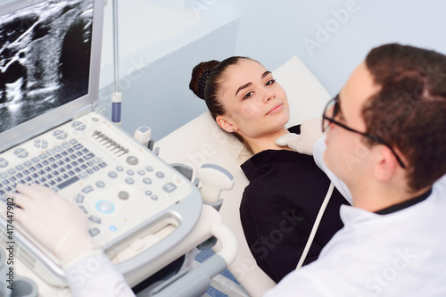 the doctor performs an ultrasound examination of the thyroid gland of a young, pretty woman in a modern clinic. Prevention of thyroid cancer.