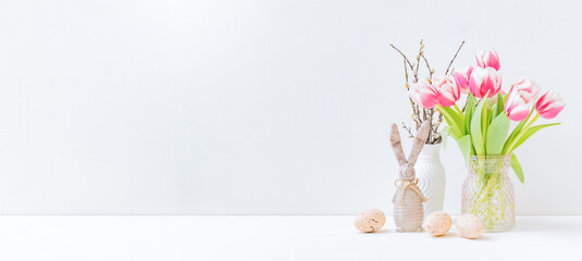 Home interior with easter decor. Pink tulips in a vase, easter eggs on a light background