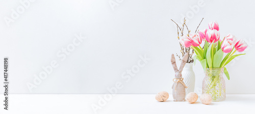 Home interior with easter decor. Pink tulips in a vase, easter eggs on a light background