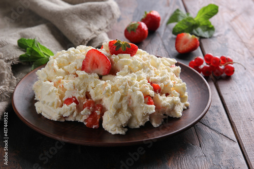 Fermented milk product. Cottage cheese with strawberries and currants in a clay plate on an old wooden background. Curd mass with mint and spoon. Rustic. Background image, copy space, horizontal