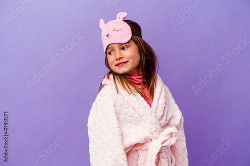 Little caucasian girl wearing pajama isolated on purple background looks aside smiling, cheerful and pleasant.