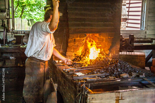 Obraz na płótnie Williamsburg, Virginia, USA - 6/23/2009: A man dressed in period clothing is demonstrating blacksmith activities in colonial Williamsburg