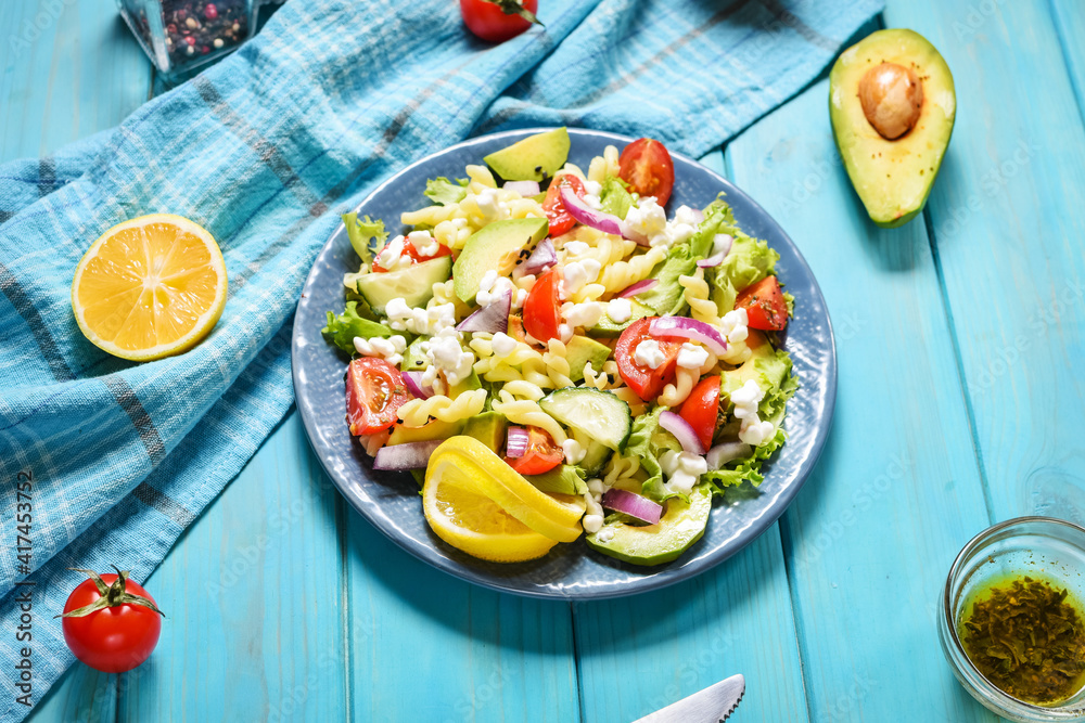 Vegetarian healthy lunch - pasta salad with fresh vegetables, avocado and feta on blue wooden background