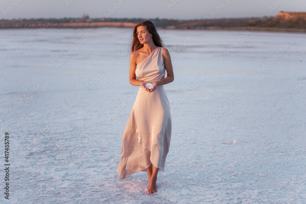 Young blonde woman in evening airy pastel pink powdery dress, holds pieces of crystallized white salt Young blonde woman in evening airy pastel pink powdery dress, holds pieces of crystallized white salt