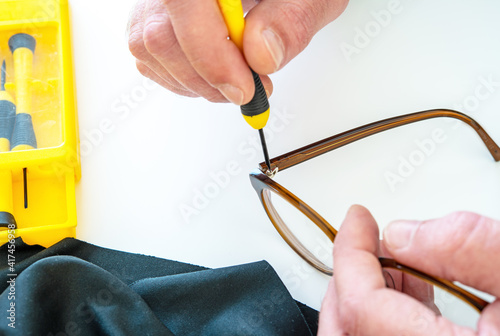 Optician repairing and fixing eye glasses with screwdriver. Hands holding a mini screwdriver tightening a loosened screw on a pair of spectacles. Optical workshop.  Maintenance and cares service.