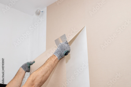 worker hand tear off old light wallpaper with scraper from wall.Repair in the apartment, removing the old wallpaper with a spatula, the process of updating the wall room repair. copy space
