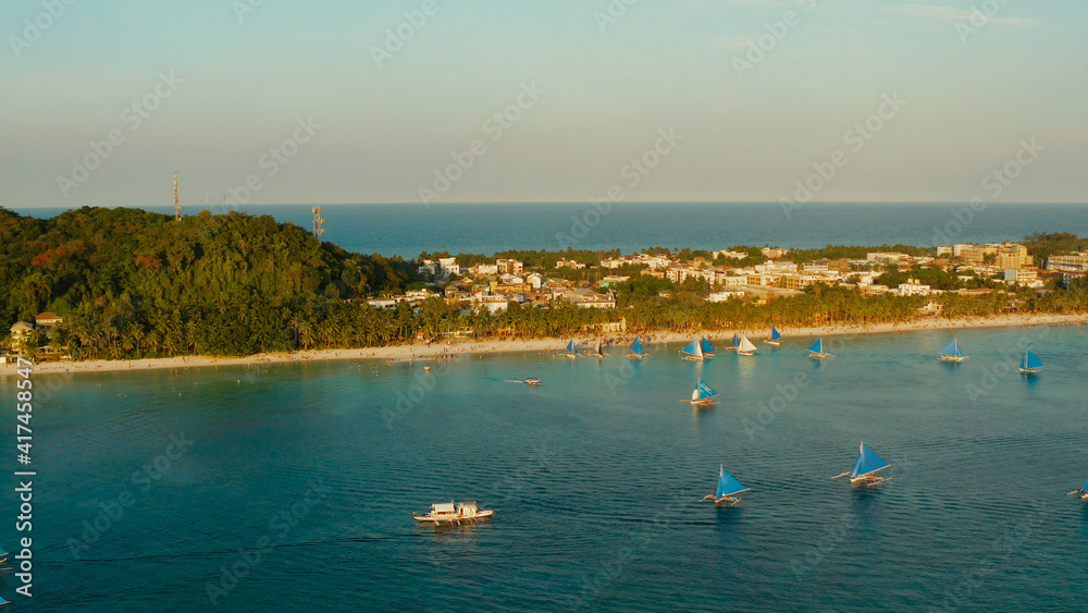 Aerial view of sailing yachts on the sandy beach of Boracay Island at sunset time. Tropical white beach with sailing boat. Summer and travel vacation concept.