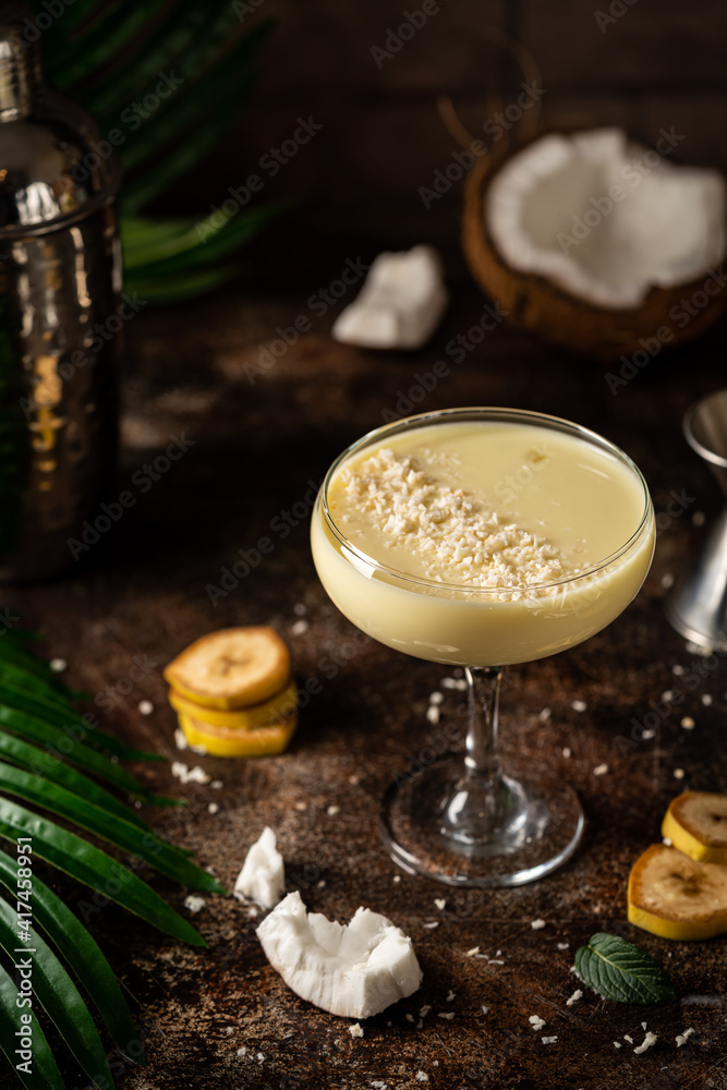 banana cocktail with coconut milk in a glass on dark background with palm leaves
