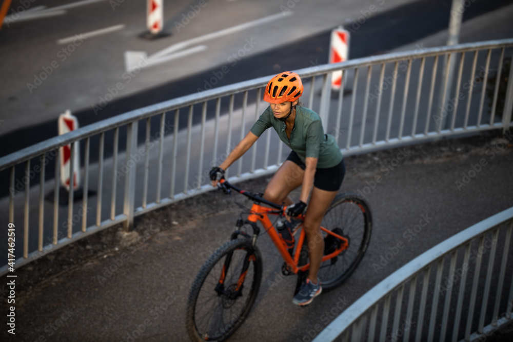 Naklejka premium Pretty, young woman with her mountain bike going for a ride past the city limits, getting the daily cardio dose