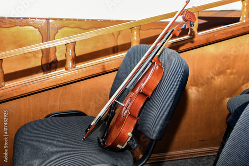 A violin with a bow and notes stands on a chair in the middle of an empty concert hall.