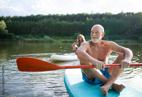Foto Senior couple paddleboarding on lake in summer.