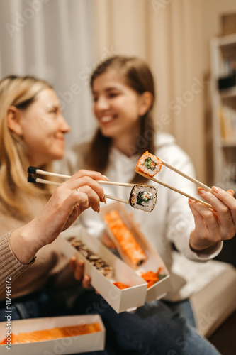 Focus on rolls. Mom and daughter are holding sushi rolls with Chinese chopsticks. Blurred background.