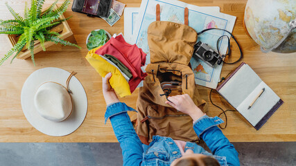 Top view of young woman packing for vacation trip holiday, desktop travel concept.