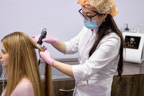 confident doctor dermatologist diagnoses structure of hair of a young woman using tool trichoscope. Trichology, trichogram, hair concept