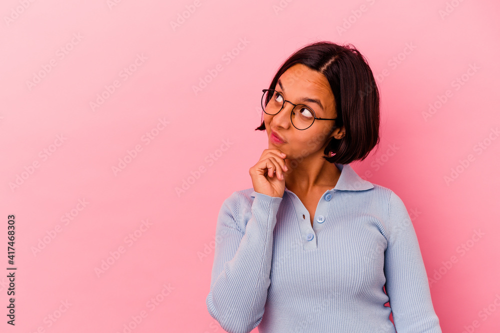 Young mixed race woman isolated on pink background relaxed thinking about something looking at a copy space. Young mixed race woman isolated on pink background relaxed thinking about something looking at a copy space.