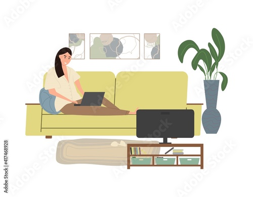 Cute young woman sitting on the couch with laptop computer in cozy room front of the TV.