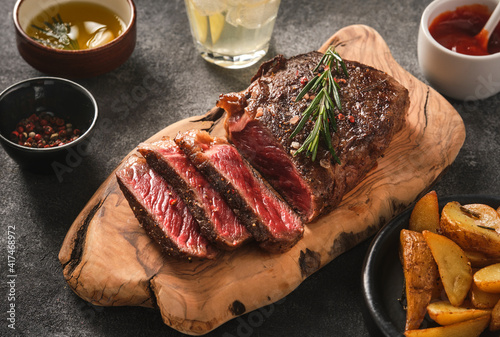 Sliced grilled meat steak New York Striploin with sauce and potato on wooden board on grey background. photo