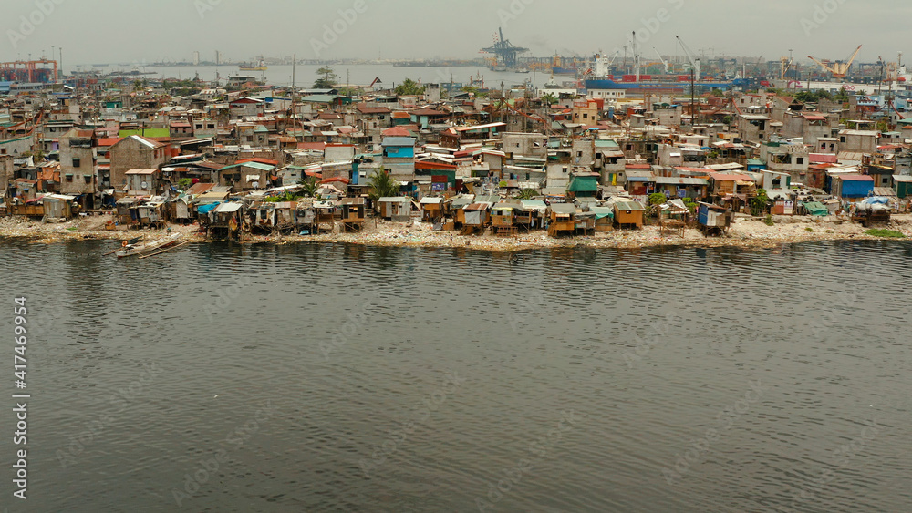 Slums in Manila near port on the bank of a river polluted with garbage, aerial view.