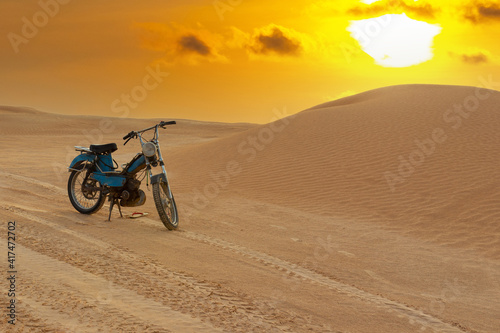 Vintage motorcycle standing in the Sahara Desert at sunset among sand dunes