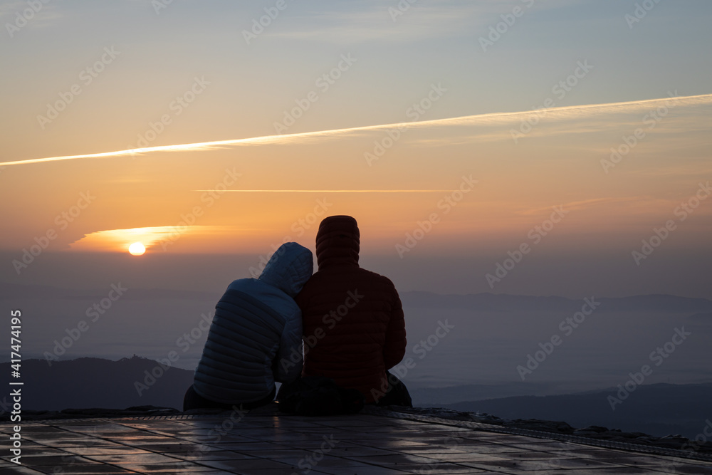 Couple watching the amazing sunrise from the top of La Mola Mountain in the Parc natural de Sant Llorenc del Munt i l'Obac, Valles Occidental, Catalonia, Spain. Copy space.