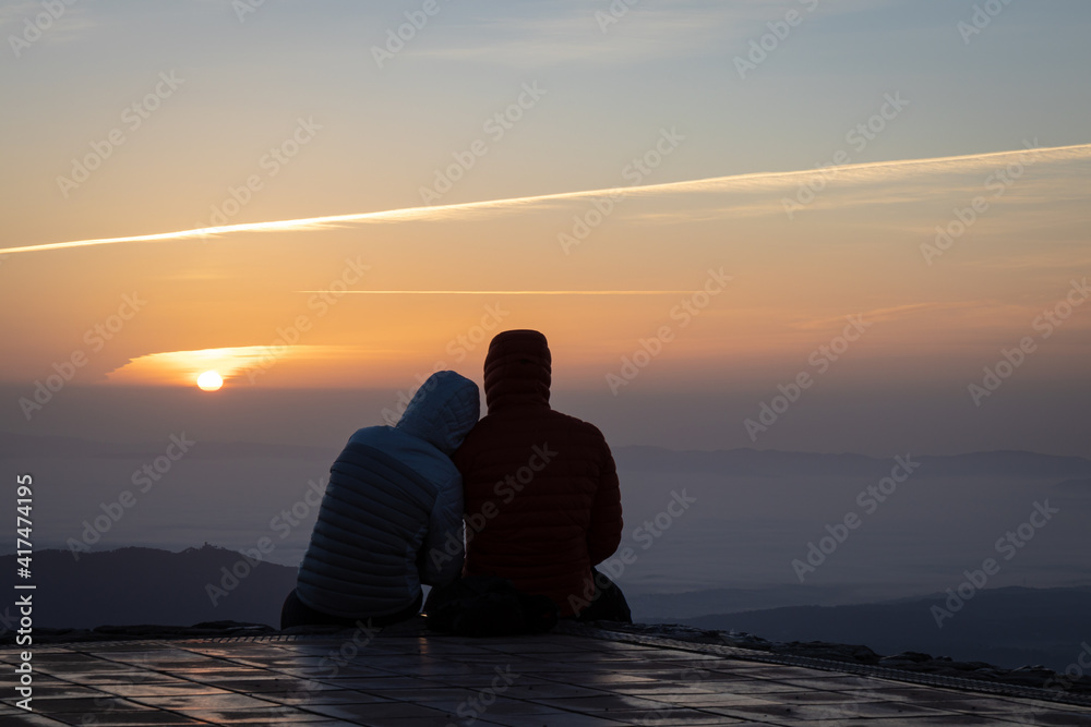 Couple watching the amazing sunrise from the top of La Mola Mountain in the Parc natural de Sant Llorenc del Munt i l'Obac, Valles Occidental, Catalonia, Spain. Copy space. Couple watching the amazing sunrise from the top of La Mola Mountain in the Parc natural de Sant Llorenc del Munt i l'Obac, Valles Occidental, Catalonia, Spain. Copy space.