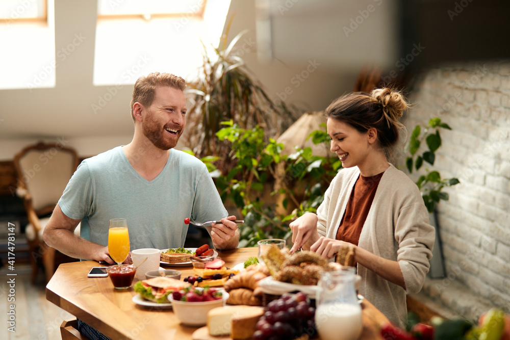 Happy couple enjoying in conversation while eating at dining table.