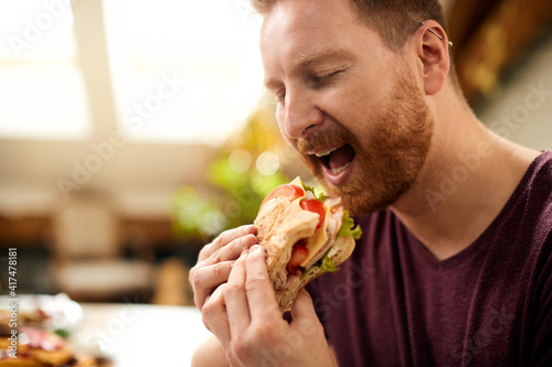 Man with eyes closed enjoying in a sandwich for breakfast at home.