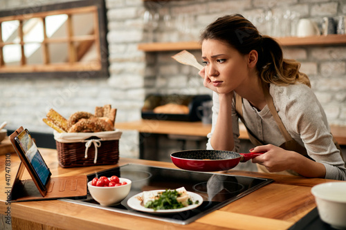 Bild auf Leinwand Young woman feeling dissatisfied while cooking and looking at recipe on the Internet