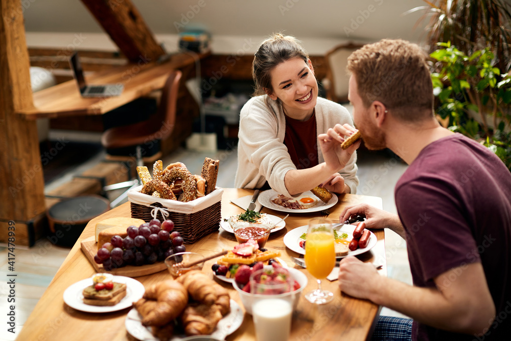 Happy woman feeding her boyfriend during breakfast at dining table.
