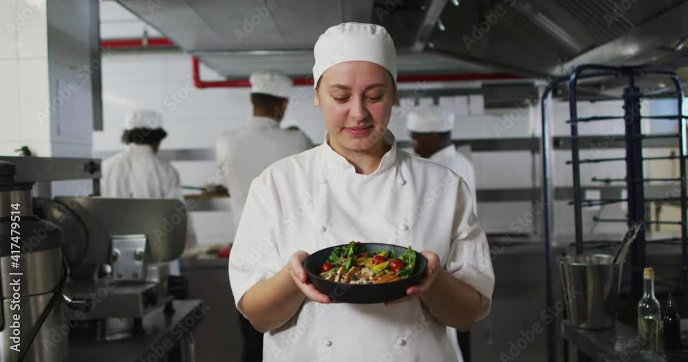 Portrait of caucasian female chef presenting dish and looking at camera
