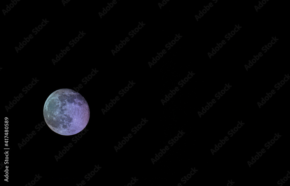 Fototapeta premium Waning multicolored moon on a dark sky. Moon with craters, isolated on black background.